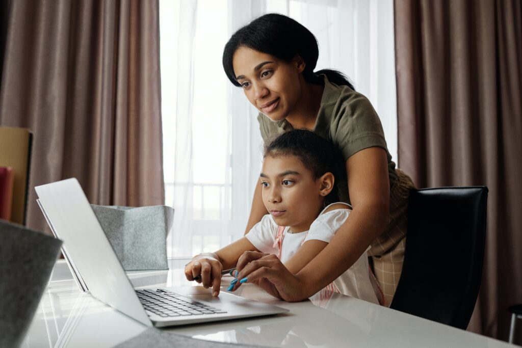 Mother teaching her daughter about laptop